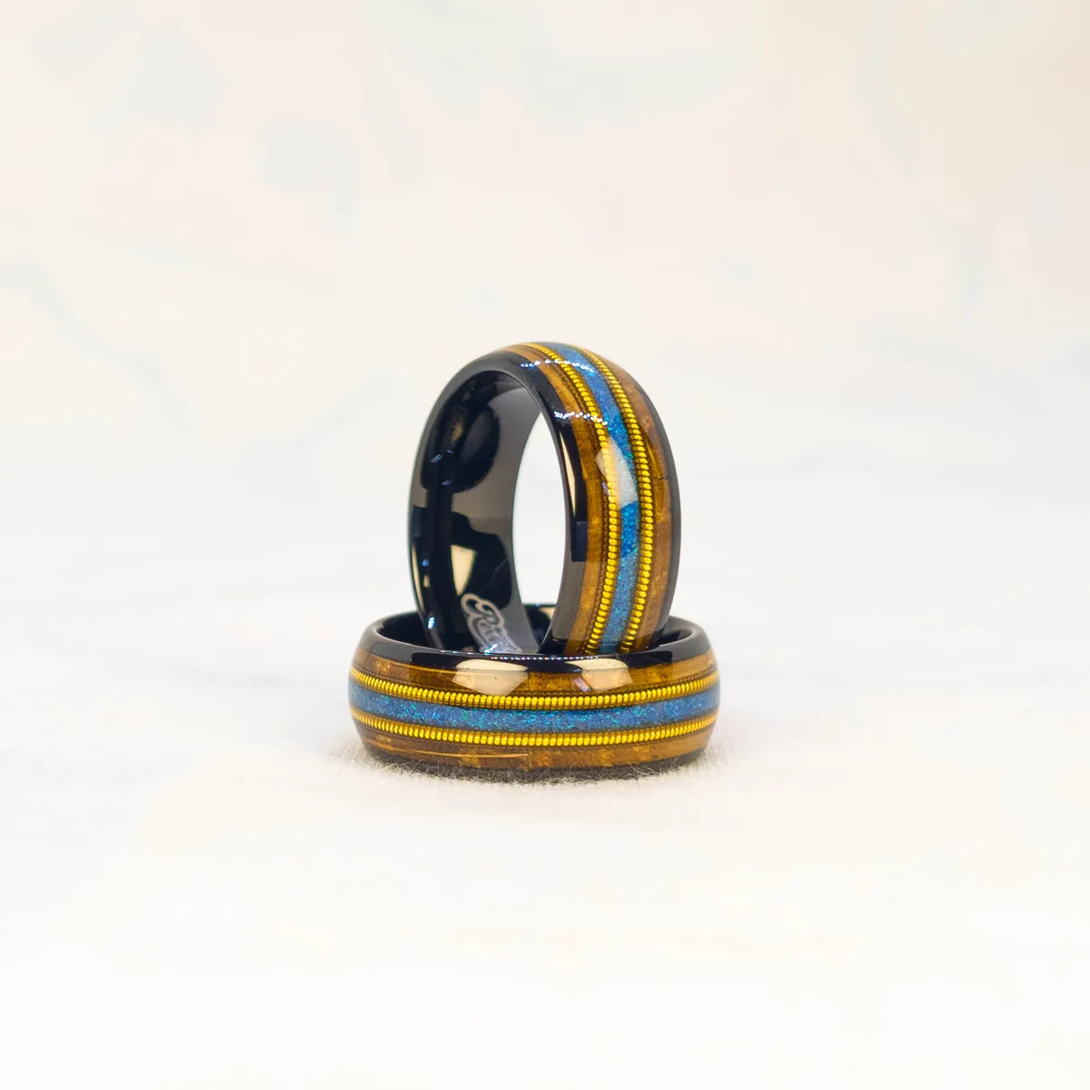 Ocean Fret Ring bright studio shot, black metal base, whiskey barrel wood inlay, golden guitar string accent