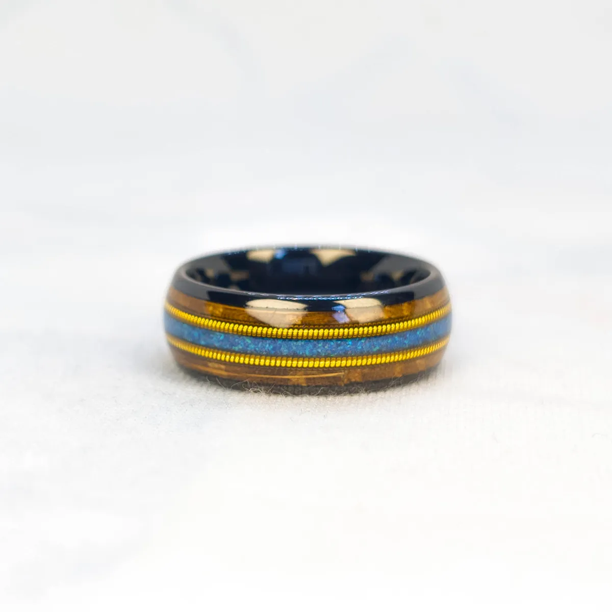 Ocean Fret Ring bright studio shot, black metal base, whiskey barrel wood inlay, golden guitar string accent