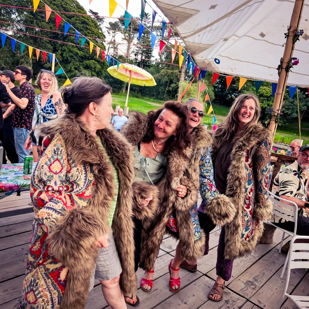 Group of people smiling and dancing while trying on colourful, fur-lined Revel Threads festival coats.