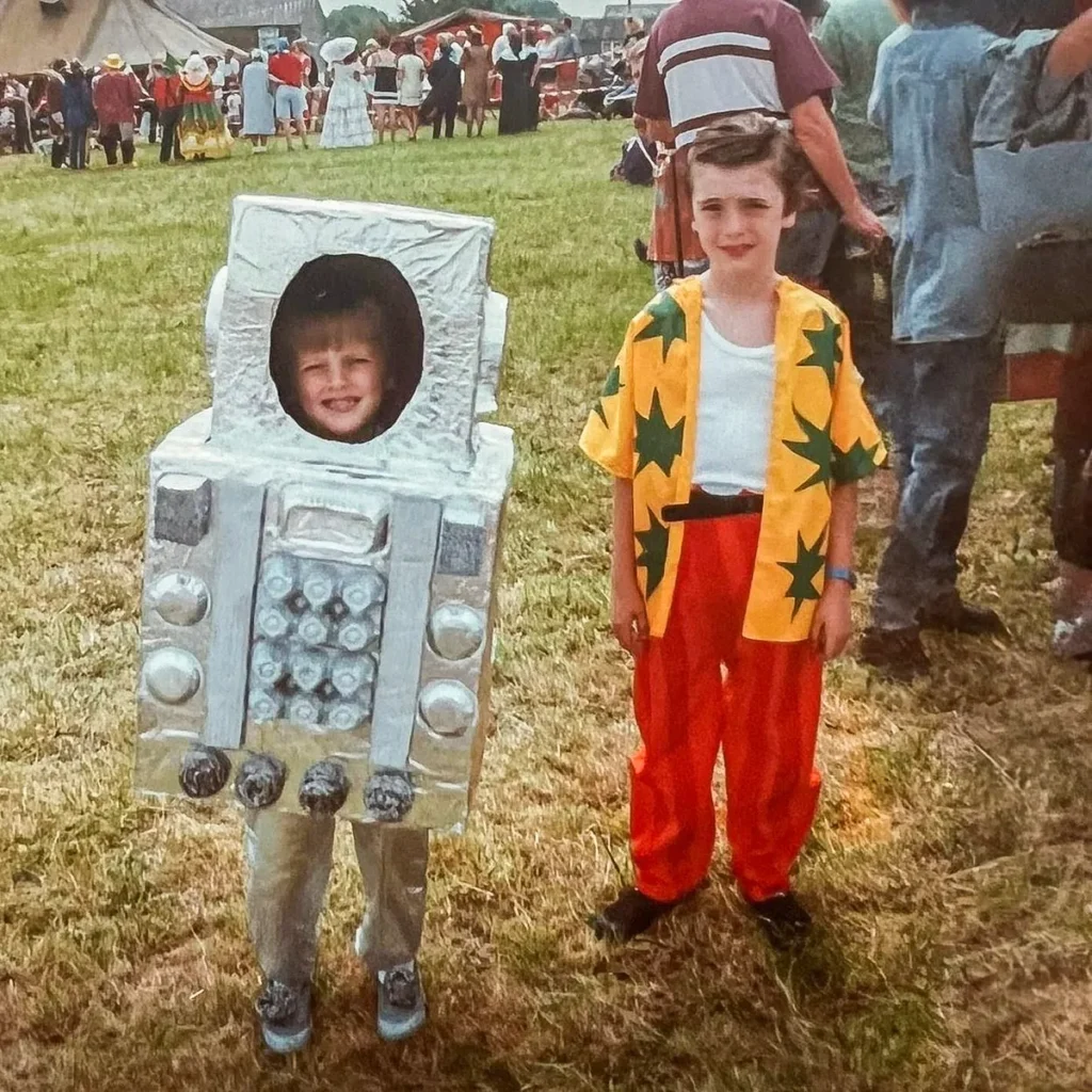 Two children at a carnival in colorful fancy dress, one dressed as Ace Ventura and the other in a homemade robot costume.