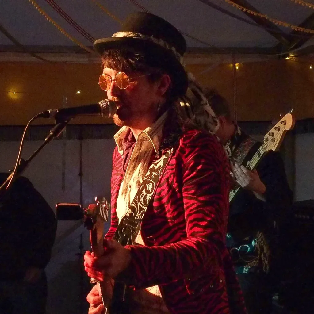 Musician performing live on stage wearing a red patterned jacket and using a handmade Sexy Strap guitar strap.